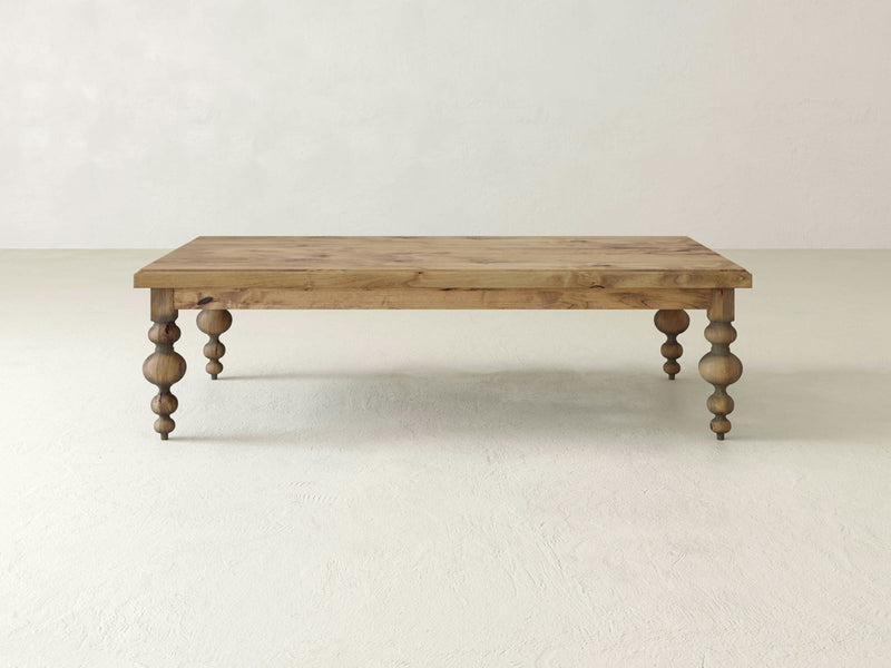 Against a plain, off-white background, the James+James Olivia Coffee Table—a rectangular wooden piece with a natural finish—makes a statement. Its four intricately carved, bulbous legs support a simple, flat top, combining minimalist design with classic charm.