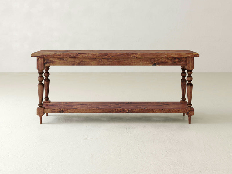 The Ella Sofa Table - Tuscany by James+James is a wooden console table featuring an upper and lower surface with four intricately carved legs. Boasting a natural wood finish, the table stands on a smooth, light-colored floor against a light background.