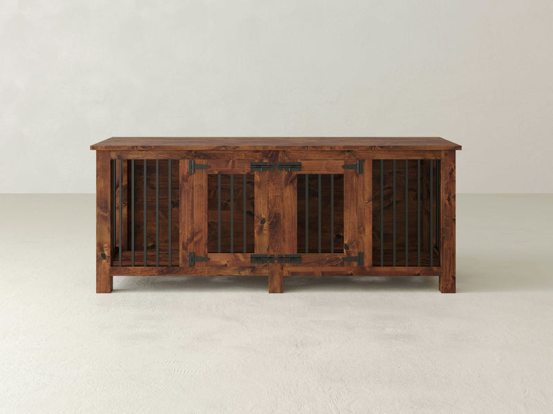 The Double Dog Kennel - Tuscany by James+James is crafted from dark-stained wood with black metal hinges and bars. This wooden pet crate features two front doors and a flat top surface, set against a plain, light-colored background.