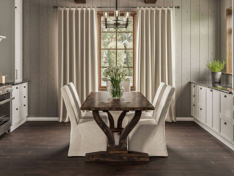 A well-lit dining room showcases the Vera Dining Table in Tobacco by James+James, paired with four beige-cushioned chairs. A vase of white tulips is centered on the table. The room features dark wooden floors and white cabinets, with a chandelier above and large window framed by beige curtains.