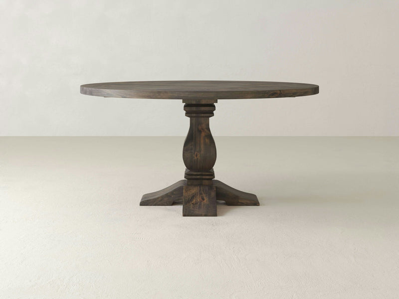 The James+James Heirloom Round Dining Table boasts timeless elegance with its dark-finish wood and a single ornate pedestal base that gracefully splits into four feet. Photographed against a plain, light-colored background, this piece adds classic charm to any dining space.