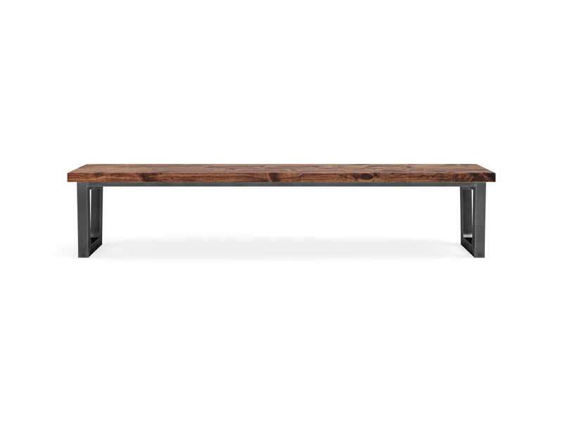 The Trapezoid Bench - Tuscany by James+James features a long, rectangular wooden seating surface with a dark brown finish, complemented by sleek black metal legs. The simple, modern design highlights the natural grain and texture of the wood, creating a clean and contemporary aesthetic that stands out against a white background.