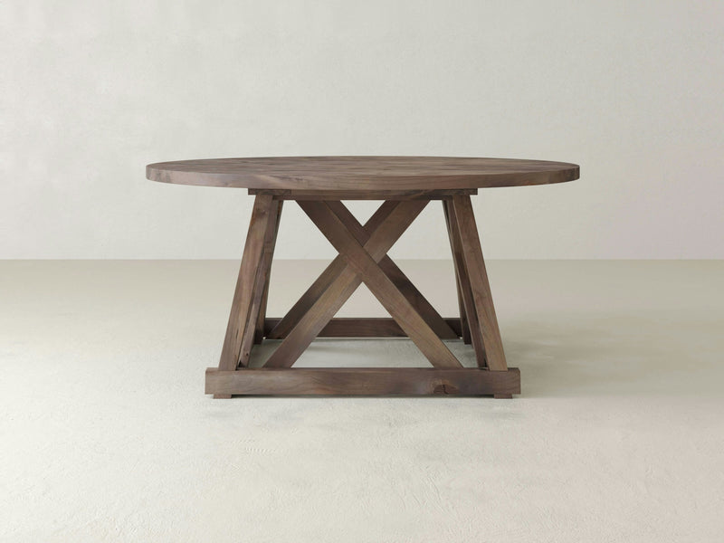 Introducing the Julia Round Dining Table - Barn Wood by James+James, featuring a natural finish and a sturdy X-shaped base. Placed against a plain, light-colored background, this table beautifully showcases its rustic yet elegant design.