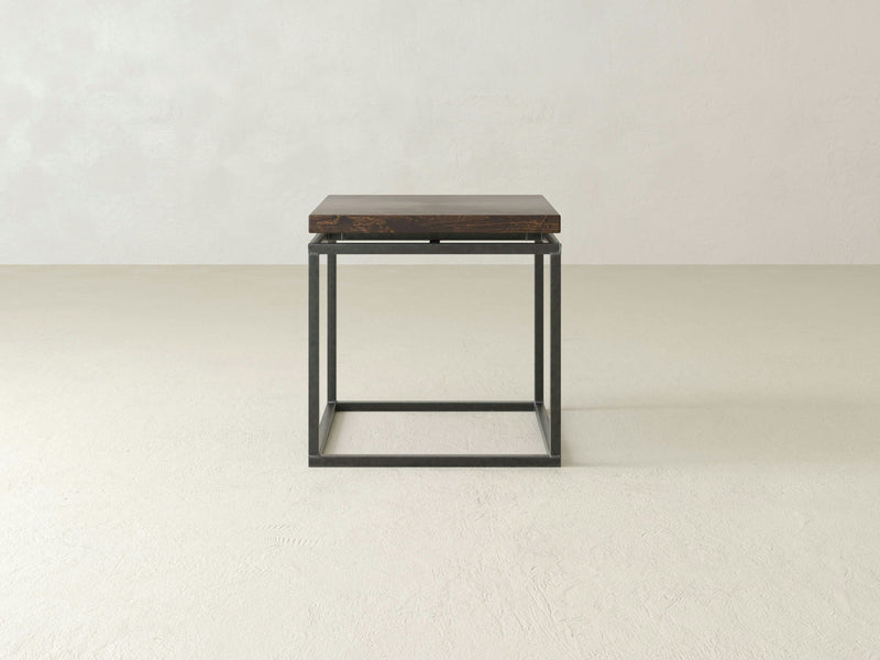 The Floating Top End Table - Tobacco by James+James, a minimalist and modern piece, features a square dark wooden top paired with a black metal frame. It sits against a plain, light-colored background showcasing its simple design with clean lines and an open base.