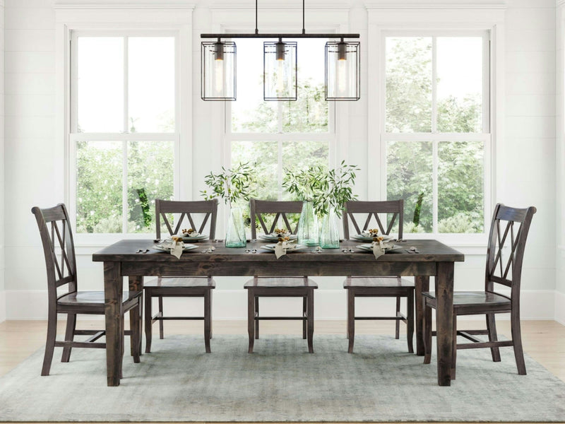 A dining room showcasing the James+James Ava Parsons Dining Table in Deep Grey, accompanied by six coordinating chairs, set atop a light blue rug. The table is beautifully decorated with greenery and table settings. Large windows in the background flood the space with natural light, while a modern black metal chandelier hangs above.