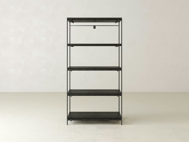 A minimalist Gwen Shelf unit from James+James, featuring five evenly spaced black metal shelves, stands against a plain white wall. The shelves are empty, and the floor is bare, emphasizing the simplicity and clean lines of this industrial design.