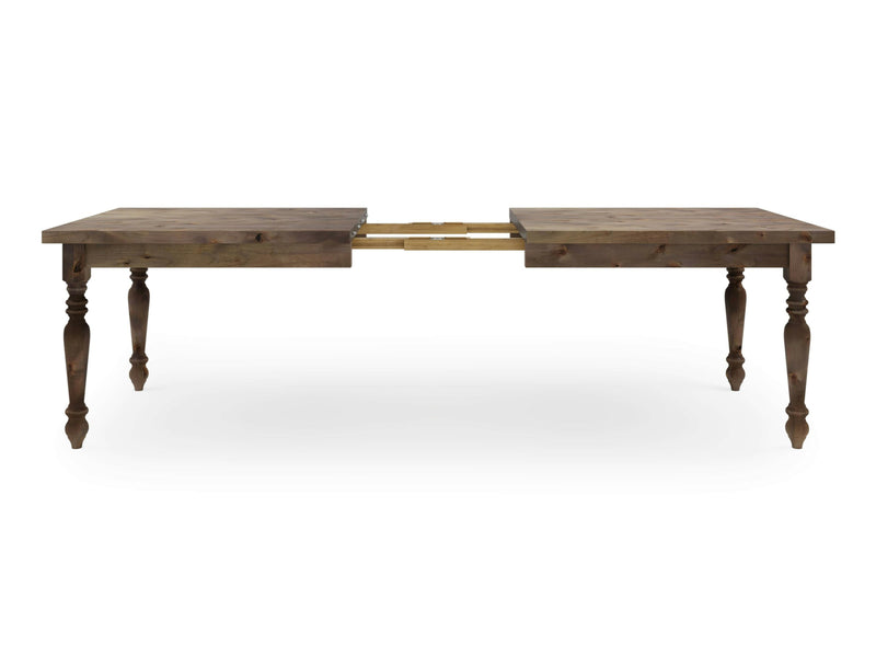 The French Country Expandable Dining Table - Barn Wood by James+James features a rectangular top and four turned legs. The table includes an extension mechanism in the middle, with the tabletop halves separated to reveal an extending leaf system. The finish is a medium brown wood tone.