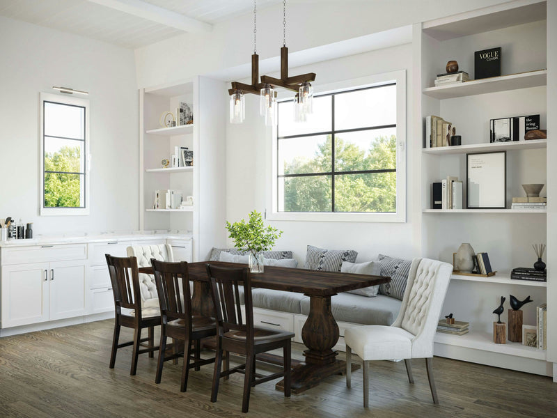 A bright, modern dining room featuring the Heirloom Expandable Dining Table in Tobacco by James+James, set for six with dark chairs and a light upholstered bench. The room boasts large windows, built-in white shelves adorned with books and decor items, and a wooden floor. A contemporary chandelier hangs elegantly above the table.