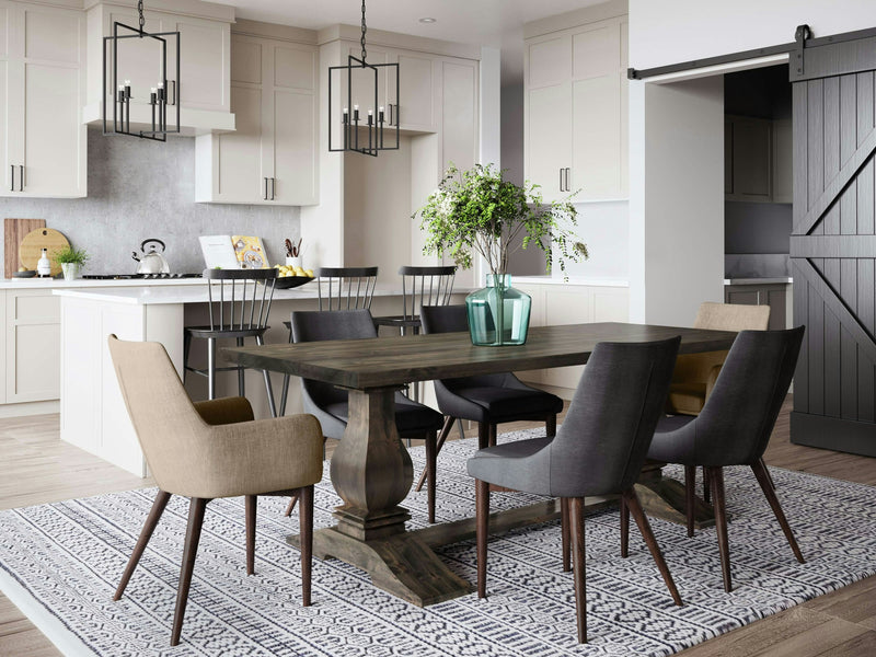 A modern dining area adjoins a kitchen with light cabinets and a gray backsplash. The Heirloom Expandable Dining Table by James+James, in Deep Grey, is surrounded by mixed beige and gray chairs, set on a patterned rug. Pendant lights hang above the table, and a barn door opens to another room.