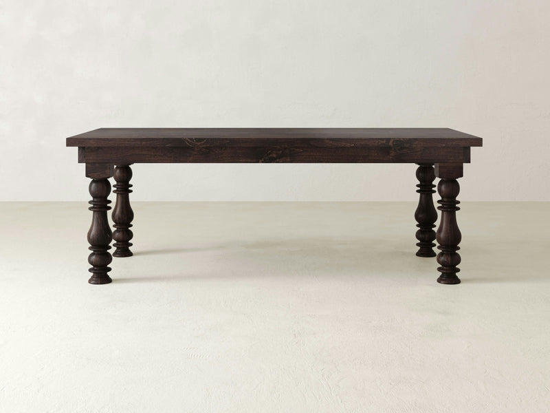 The Annli Dining Table - Tobacco by James+James stands on a light-colored floor against a plain light-colored background. This rectangular wooden table, boasting a dark brown finish, features four ornately turned legs and a simple, smooth tabletop that exudes a classic and timeless look.