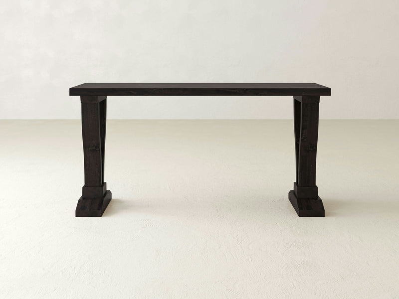 The Vera Sofa Table by James+James is a sophisticated black wooden console table that highlights exquisite artisanal craftsmanship and a clean, minimalist design. This elegant piece features two solid, rectangular legs with subtly flared bases, beautifully displayed against a plain white background.