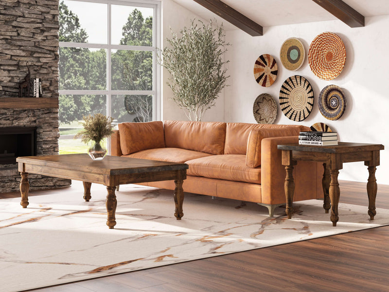 A spacious living room featuring a brown leather sofa, a wooden coffee table, and an Abigail End Table - Tuscany from James+James. The setting is complete with a large window, stone fireplace, a floor-length light rug with brown patterns, and walls adorned with circular woven decorative pieces in various designs and colors.