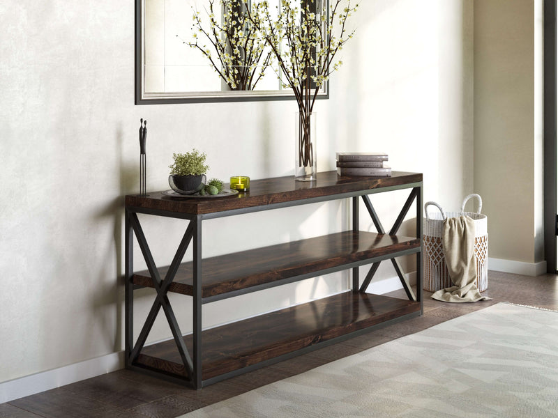 The Boyd Shelf by James+James, with its modern dark wood and industrial steel frame, stands against a light wall. It holds a vase with branches, two small books, a candle, and a potted plant. A large mirror is mounted above it, and a woven basket sits beside it on the floor.