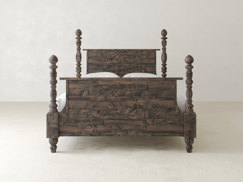 The Catherine Bed by James+James, made from hardwood with intricately carved posts and a dark finish, stands elegantly on a light-colored floor against an off-white wall. Its simple headboard and footboard exude vintage sophistication in a timeless design.