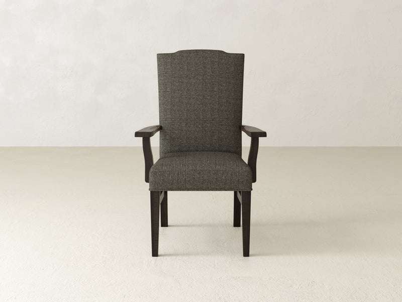 A Hadley Arm Dining Chair in Charred Ember by James+James, featuring a textured fabric design and wooden armrests and legs, is centered against a plain light background.