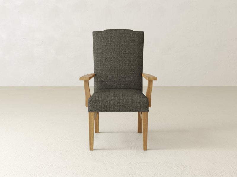 A Hadley Arm Dining Chair in the Harvest Wheat finish by James+James, featuring a tall backrest and armrests, upholstered in dark gray fabric, is placed against a plain, light-colored background.