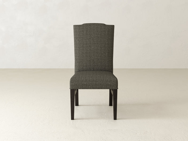 The Hadley Side Dining Chair by James+James, featuring a high back and dark wooden legs, set against a light beige background, enhances your dining experience with its simple yet elegant upholstered fabric design.