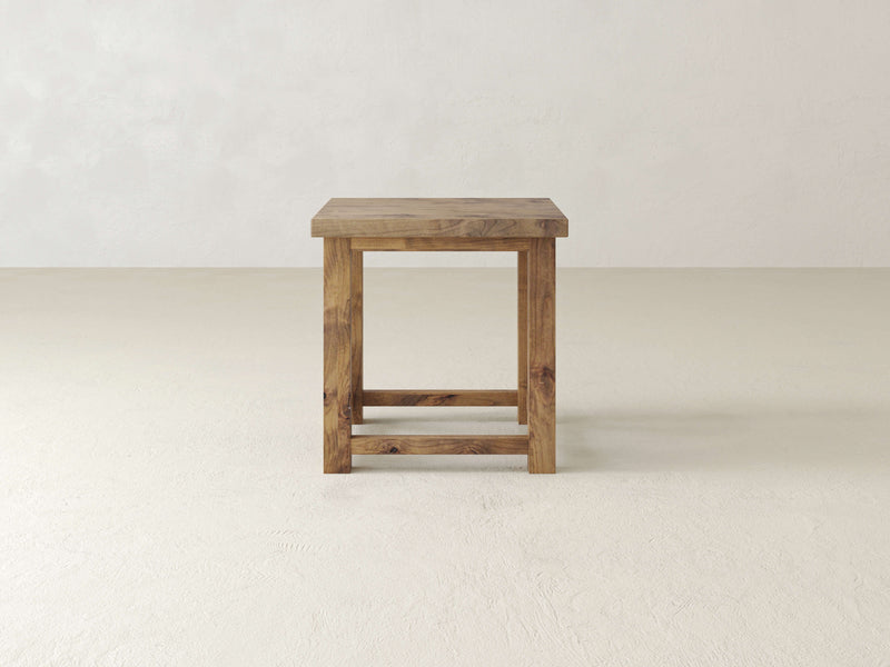 Close-up of the Carter X Side Table - Harvest Wheat by James+James, highlighting its wood surface with natural grain patterns. The table's smooth texture features a knot and a crack towards the upper right corner, displaying varying shades of brown and subtle, flowing lines throughout.