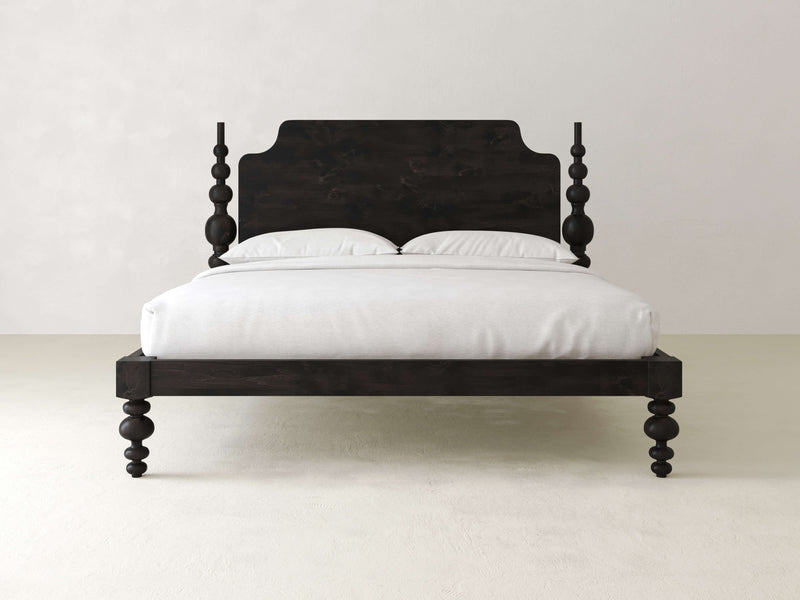 The Opal Bed - Charred Ember by James+James, a dark wooden four-poster bed with a high headboard and decorative posts, is elegantly adorned with a white mattress and pillows, set against a plain white wall.