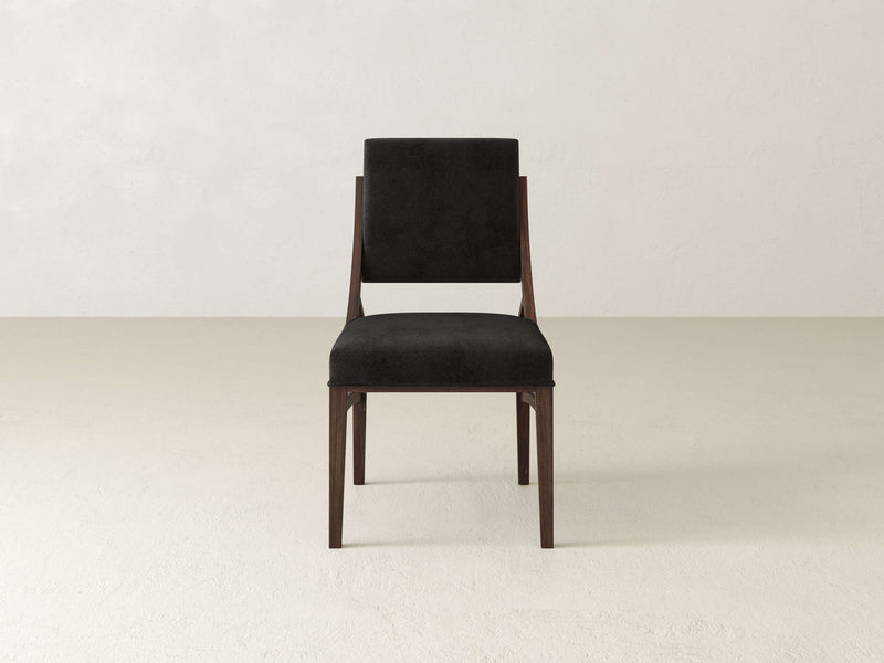 The Quinn Dining Chair - Tobacco by James+James, a minimalist wooden chair with a black cushioned seat and backrest, is set against a plain, off-white background. The chair boasts a sleek and modern design with clean lines and a rectangular backrest.