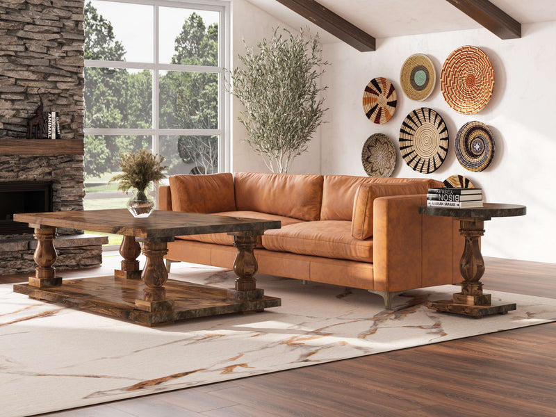 A cozy living room features a caramel leather sofa, a wooden coffee table, and matching Vivien Side Tables by James+James in Tuscany finish. Decorative woven baskets adorn a white wall, while large windows let in natural light. The room has a stone fireplace and a light rug with brown and white patterns.