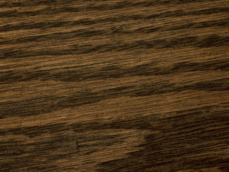 Close-up of the textured surface of the White Oak Buffet - Charred Ember by James+James, showcasing natural grain patterns running horizontally. The wood displays shades of dark brown with lighter streaks, emphasizing the organic and rustic appearance of this exquisite piece.