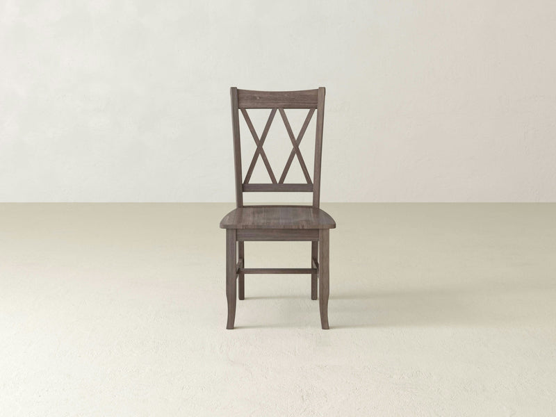 A James+James Double X-Back Dining Chair - Barn Wood is centered against a light beige background. The chair, with its dark brown finish, features a straight backrest adorned with a double cross-pattern design and a flat seat. The overall design is simple and classic.