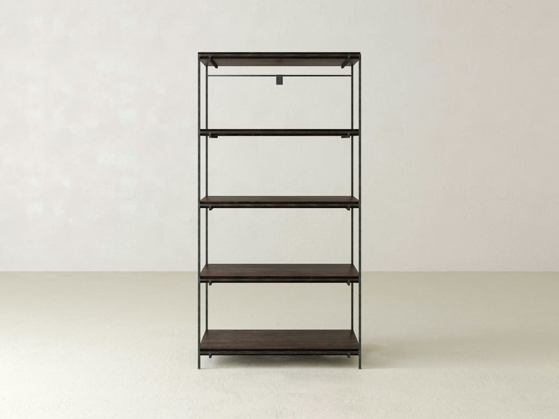 The Gwen Shelf by James+James is a minimalist, freestanding shelving unit featuring a black metal frame and five solid hardwood shelves. Positioned against a plain, light-colored wall and set on a clean, white floor, its industrial design is simple and functional, perfectly suited for various storage needs.