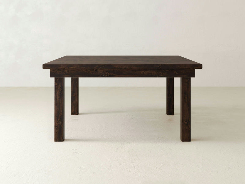 The Farmhouse Square Dining Table - Tobacco by James+James is set against a plain white background, featuring a dark wooden finish with a sturdy rectangular top and four straight legs. The table boasts a simple, minimalist design and appears well-built, making it suitable for various dining or workspace settings.