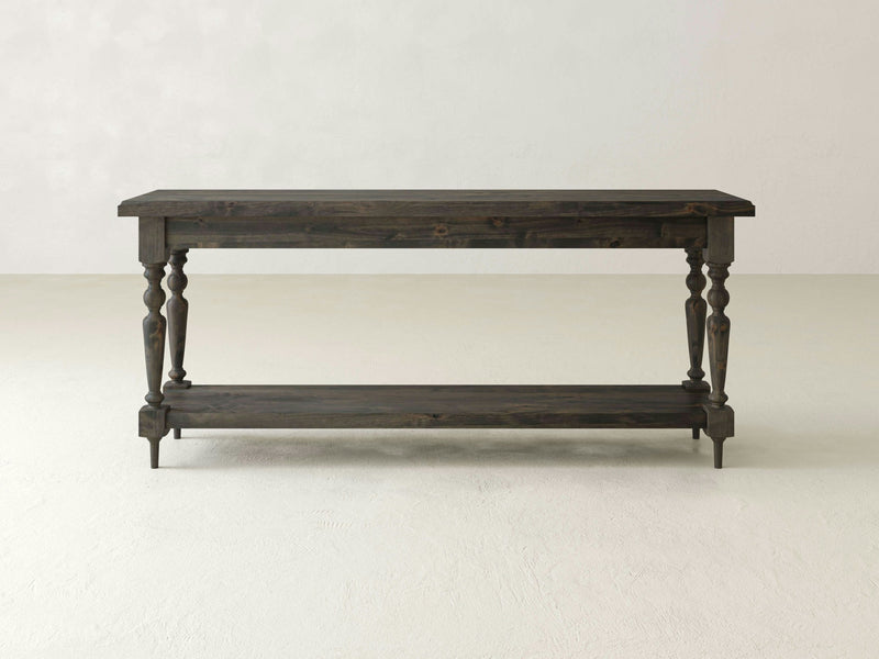 The Ella Sofa Table by James+James features a deep grey finish with a rectangular top and ornate, turned legs. This elegant piece includes an additional lower shelf for storage, all in a matching wood finish. Its traditional design makes it suitable for a variety of decors.