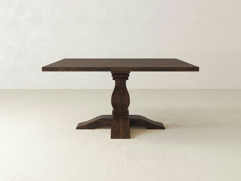 A Heirloom Square Dining Table - Tobacco from James+James, featuring a dark wooden finish and a single ornate pedestal base, is centered against a light, plain background. The design is simple yet elegant, with clean lines and a rustic finish.