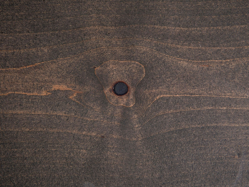 Close-up of the Nora Buffet - Deep Grey by James+James, showcasing its wooden surface with a distinct knot in the center. The wood grain forms natural, wavy patterns around the knot, varying in shades of brown. The texture is visibly smooth, highlighting the organic characteristics of the wood.