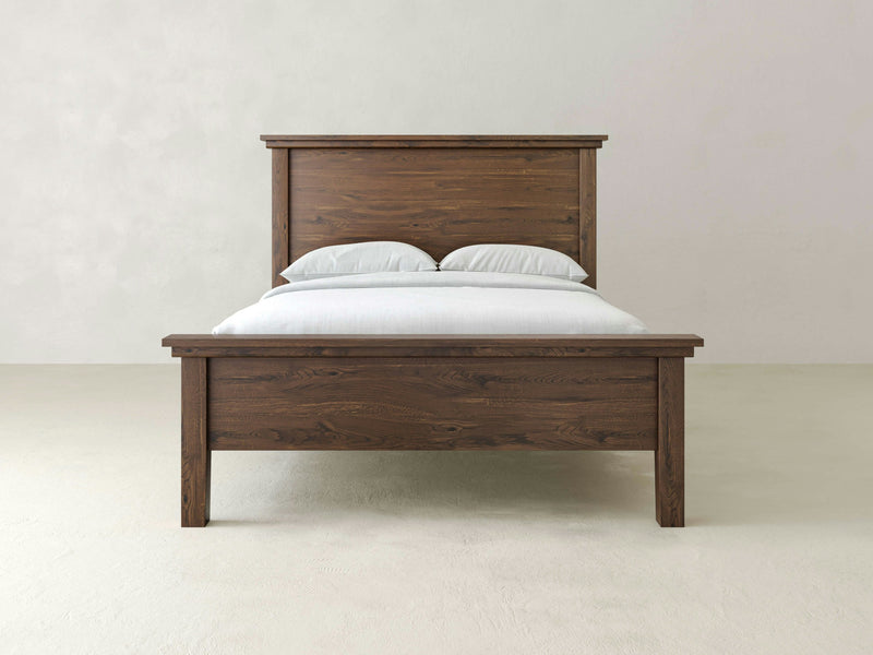 An Ivy Bed - Deep Grey from James+James with a simple design is centered in the image. It features a smooth headboard and footboard made of deep grey wood. The bed is neatly made with white bedding, consisting of two pillows and a plain white blanket. The background is plain and light-colored.