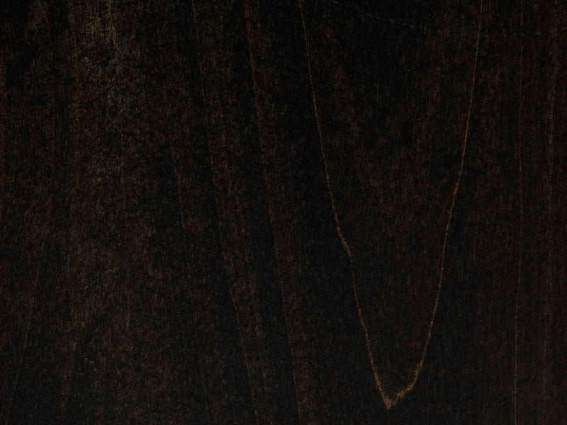 A close-up of the Charred Ember on Alder Sample by James+James reveals a dark, textured surface with subtle variations in color and grain patterns. A faint V-shaped lighter streak adds depth to the otherwise rich and smooth finish, which has a deep, almost black appearance.