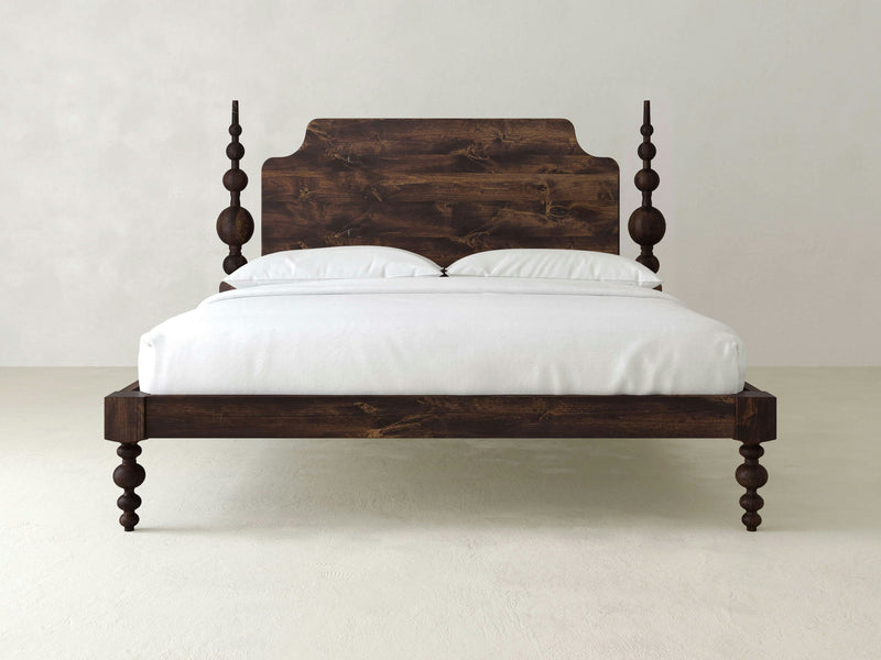 The Opal Bed - Tobacco by James+James features an intricately carved headboard and bedposts with a dark brown finish. It is neatly made with white sheets and two white pillows, set against a plain, light-colored background.