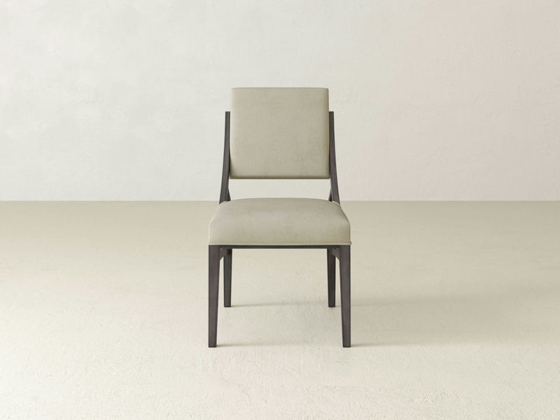 The Quinn Dining Chair - Deep Grey from James+James, featuring a simple, modern design with a beige cushioned seat and backrest, sits on a plain, light-colored floor against a light wall. The chair's minimalist aesthetic is complemented by its dark, thin frame.