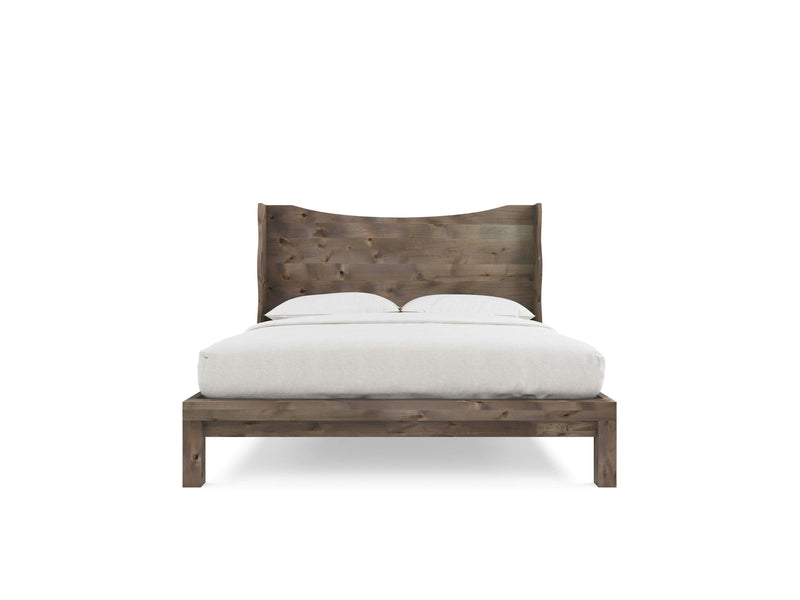 The Harlow Bed - Barn Wood by James+James showcases a distinctly curved headboard and a natural wood finish. It's neatly made with white bedding, including a comforter and two pillows. The overall design is minimalist, set against a plain white background.