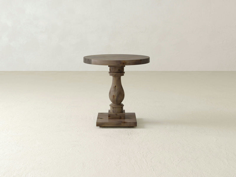 The Vivien Side Table by James+James showcases a slender, intricately carved pedestal leg and a square base, set against a plain, light-colored background.