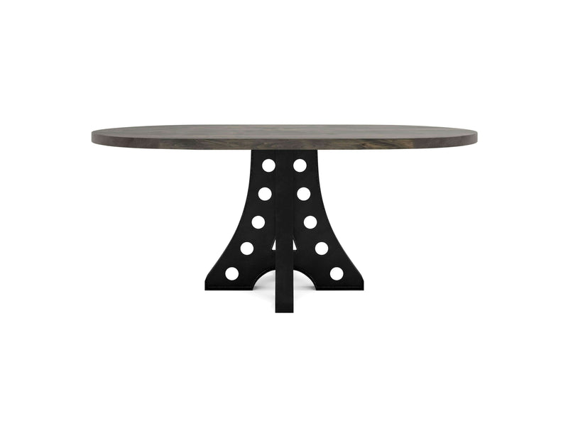 The Amelia Oval Dining Table - Deep Grey by James+James features a thick wooden tabletop and a distinctive black pedestal base with large circular cutouts. This design blends rustic and industrial elements, creating a modern and visually striking piece of furniture.