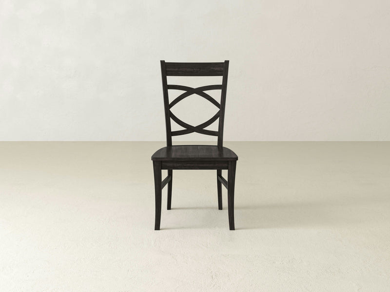 The Ansley Dining Chair by James+James, crafted from dark wood and highlighted by a decorative crisscross pattern on its backrest, is centered against a plain, off-white background. This elegant chair features four straight legs and a rectangular seat, ensuring both style and sturdy build.