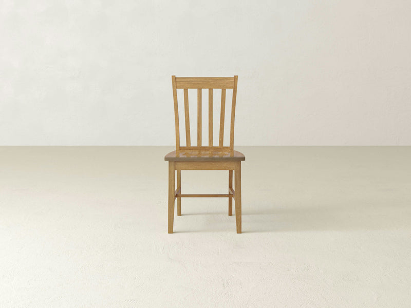 A Henry Dining Chair - Harvest Wheat by James+James is centered in an empty room with light-colored walls and a beige floor. The chair features a straight back with vertical slats and a flat seat. Its overall design is minimalist and functional.