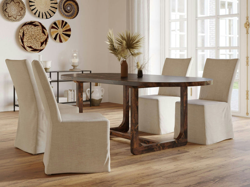 A minimalist dining room features the Emersen Oval Dining Table in Tobacco from James+James, surrounded by four beige upholstered chairs. The space is adorned with wicker baskets on the wall, two ceramic vases filled with dried plants on the table, and large windows that flood the room with natural light.