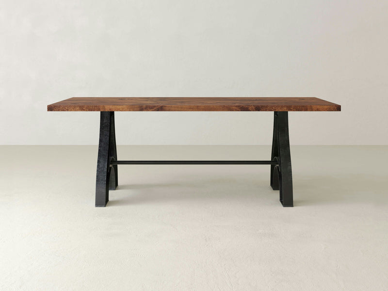 The Wishbone Dining Table - Tuscany by James+James features a polished rectangular wooden surface paired with a sturdy, black metal base. This stand-alone piece is set against a plain, light-colored background, highlighting its modern design and natural wood grain.