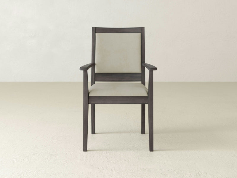 The Gina Arm Dining Chair by James+James, featuring a deep grey frame and light-colored cushioned seat and backrest, is positioned against a plain, light background. The simple design includes straight lines and armrests.