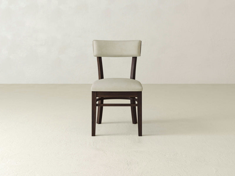 The Everly Side Dining Chair - Tobacco by James+James, featuring a dark brown frame and beige cushioned seat and backrest, is positioned against a plain, light-colored wall on a light-colored floor. The chair boasts a simple, modern design.