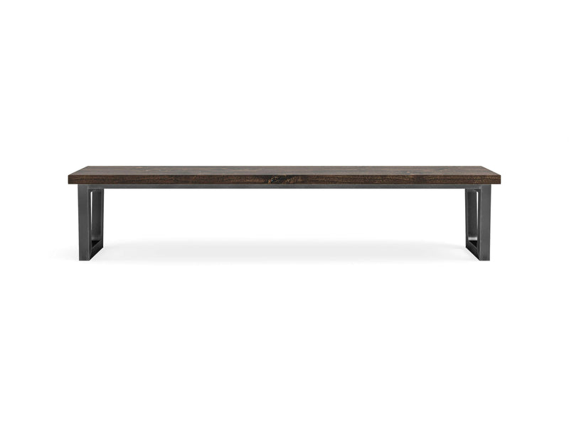 The Trapezoid Bench - Tobacco by James+James is a minimalist rectangular bench featuring a dark wooden top and black metal legs. The design showcases clean, straight lines with a modern, industrial aesthetic, all set against a simple white background.