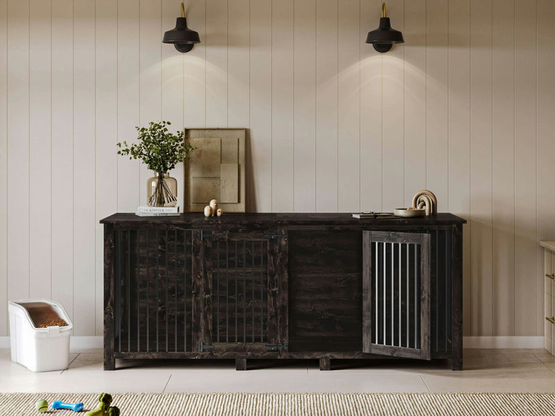 A sleek Double Dog Kennel in Charred Ember from James+James is set against a light panel wall, featuring two black metal lantern-style wall sconces above. On the kennel, there are plants and framed pictures. Nearby, a small pet litter box is visible on the floor, along with a few scattered toys.