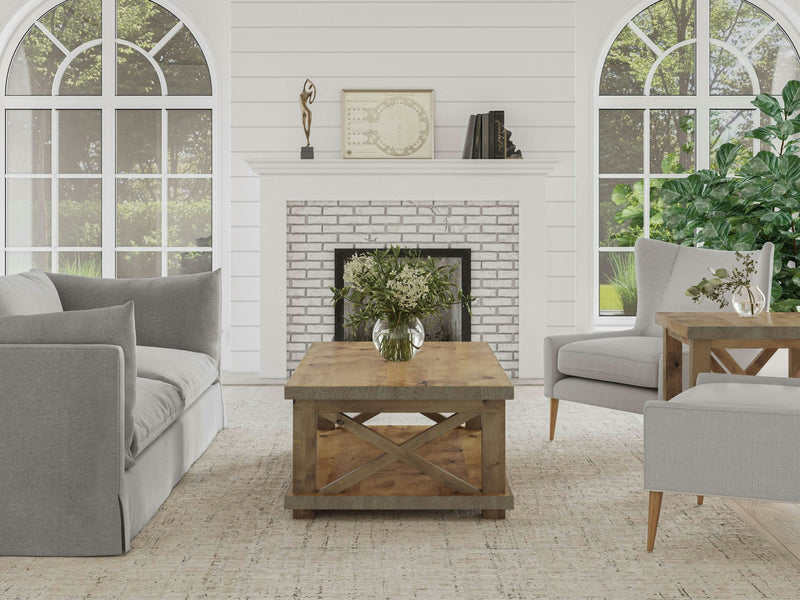 A cozy living room with a modern farmhouse style. It features a grey sofa and armchair, a Carter X Coffee Table in Harvest Wheat by James+James, and a fireplace with a white brick surround. Two large arched windows bring in natural light, and a vase with flowers sits on the coffee table.