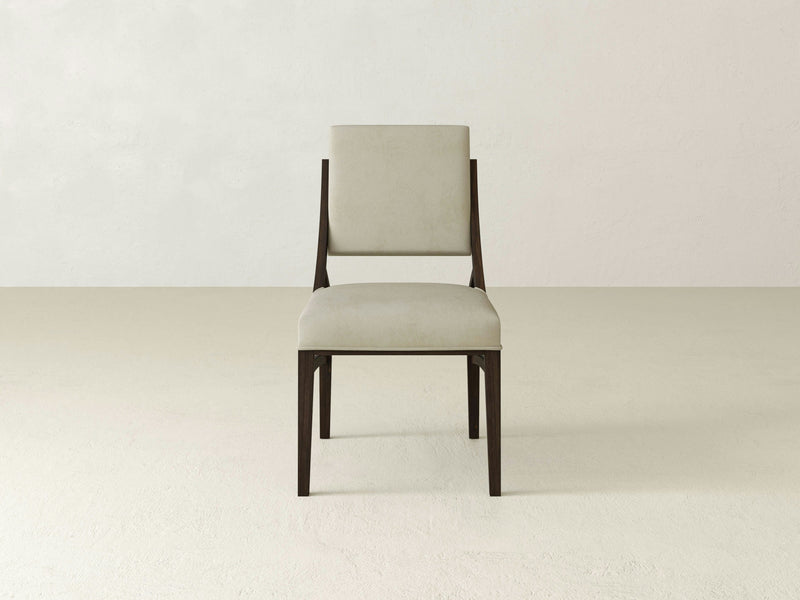 A single Quinn Dining Chair - Tobacco by James+James, featuring light beige upholstery on the seat and backrest, is positioned against a plain, light-colored wall and floor. The chair showcases a simple, modern design.