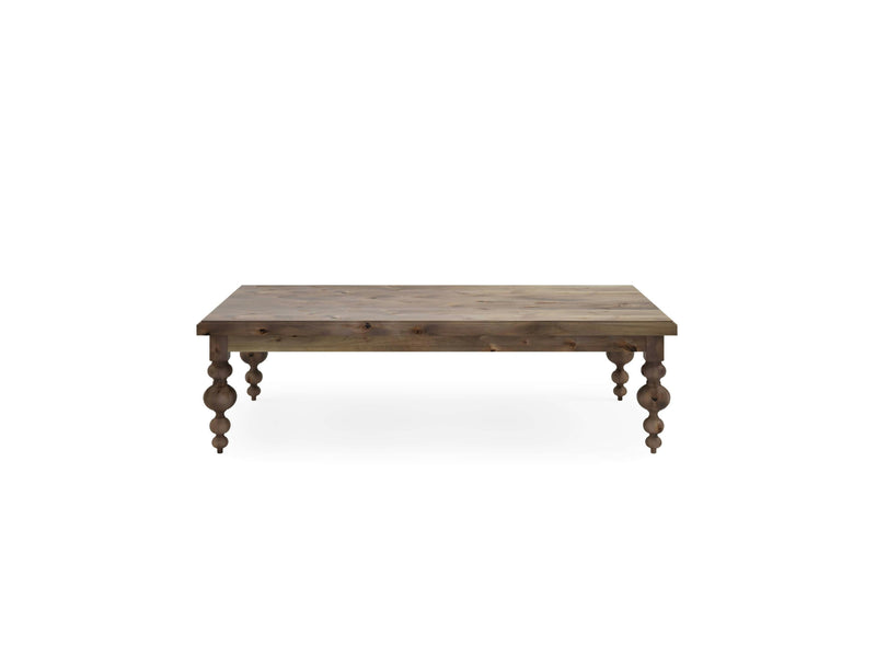 The Olivia Coffee Table by James+James is a rectangular wooden piece with a barn wood finish. It has a plain, slightly distressed top surface and features intricately carved, spindle-style legs. The table's rustic and classic design makes it an ideal addition to any living room or kitchen.